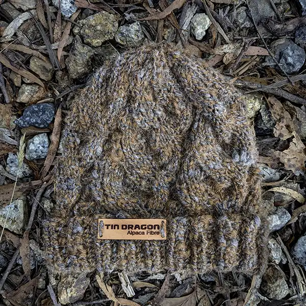 Charcoal-brown-cable beanie lying on large gravel surface
