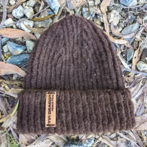 A hand-knitted brown alpaca beanie is on a gravel backgound