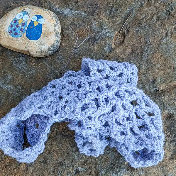 A lavender alpaca scarf is on a large brown rock