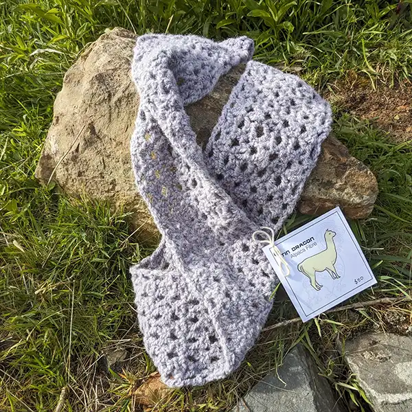 A lavender-coloured alpaca scarf is displayed on a rock in a garden