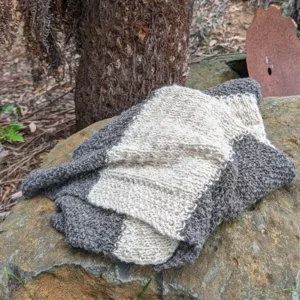 Hand-knitted pure alpaca charcoal and cream blanket lying on a large rock.