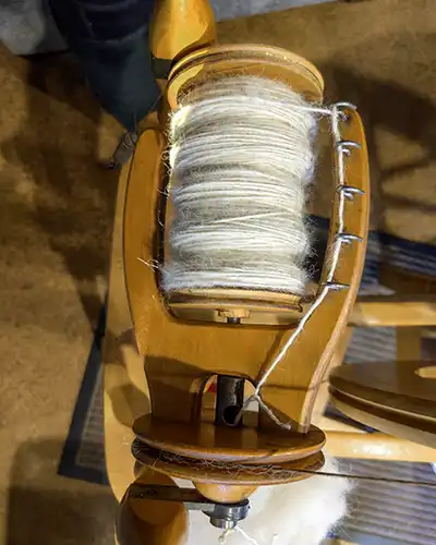 A spinning wheel bobbin is filled with white alpaca fibre single thread